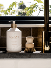 L'AVANT Collective - High Performing Dish Soap - Blushed Bergamot in a matte white bottle next to a brush on a counter.