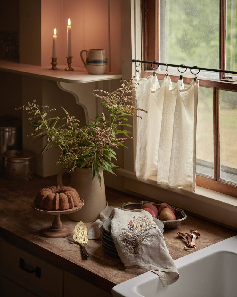 Wheat Harvest Tea Towel by Coral & Tusk on a rustic kitchen counter, adorned with a bundt cake, pears, and a decorative metal cake server.