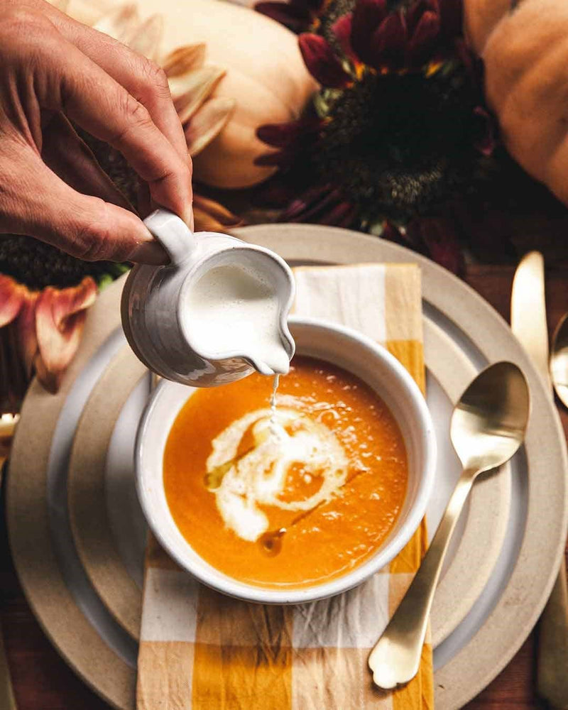 Farmhouse Pottery - Bell Pitcher elegantly pours cream into a bowl of autumn soup, showcasing its classic form and functional charm in a cozy table setting.