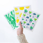 Bespoke Provisions - Tropical Leaves Swedish Dishcloth held in hand, featuring plant and lemon drawings, hygienic alternative to sponges, biodegradable, suitable for cleaning various surfaces.