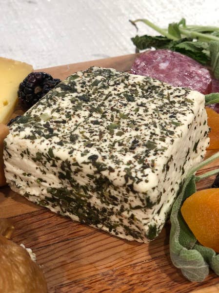 Tulip Tree Creamery - Nettle cheese block coated in herbs, paired with salami, firm cheese wedge, dried apricots, and blackberry, showcasing a curated charcuterie selection.