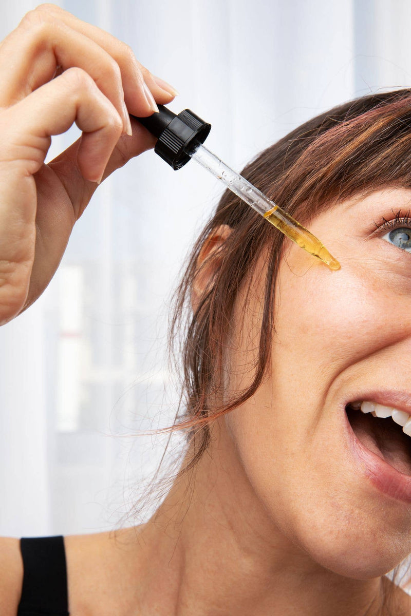 Close-up of a person applying Roots And Leaves - Organic Facial Serum & Cleanser with a dropper, highlighting its nourishing, natural formula for radiant skin.