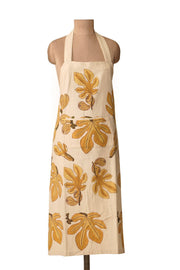 Couleur Nature - Fig Citrine Apron: Cream apron with stylized yellow-orange fig leaves and fruit, halter neck strap, and front patch pocket, ideal for kitchen use.