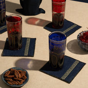 ATELIER SAUCIER - Grecian Cocktail Napkins accompany ornate glasses and snacks, showcasing geometric motif and golden trim on a light-beige surface.