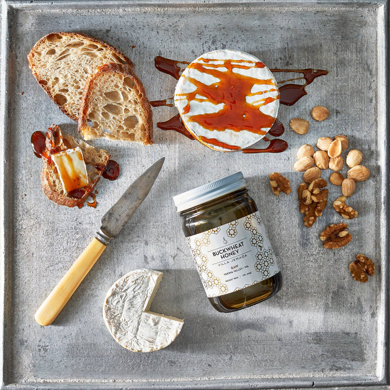 Villa Jerada - Buckwheat Honey - 1lb jar with cheese, sourdough, and nuts on a baking sheet, showcasing a sweet-and-savory pairing.