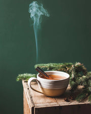 Farmhouse Pottery - Pantry Mug: Large, filled with steaming spiced drink, cinnamon stick, on wooden box with evergreen sprigs and pine cones, showcasing rustic charm and versatility.