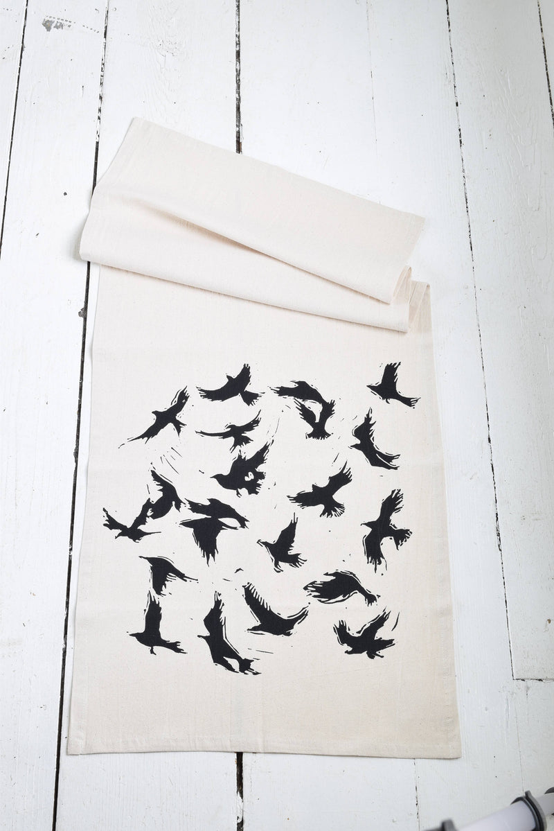 Hearth and Harrow - Organic Cotton Flying Crows Tea Towel featuring black bird silhouettes, designed and hand-printed with eco-friendly ink, laid on a wooden surface.