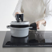 A person lifts a pot lid using Yamazaki Home Magnetic Pot Holders, Silicone, Black, showcasing safe, heat-resistant handling on a sleek cooktop.