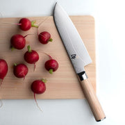 Shun | Classic Blonde Santoku, 7 knife displayed on light-wood cutting board with radishes; features patterned stainless blade and blonde Pakkawood handle, embodying versatility and precision.