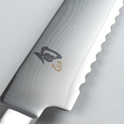 Close-up of Shun Classic Bread Ebony knife blade, showcasing Damascus-style waves, scalloped serrations for effective bread slicing, and a black and gold maker’s mark.