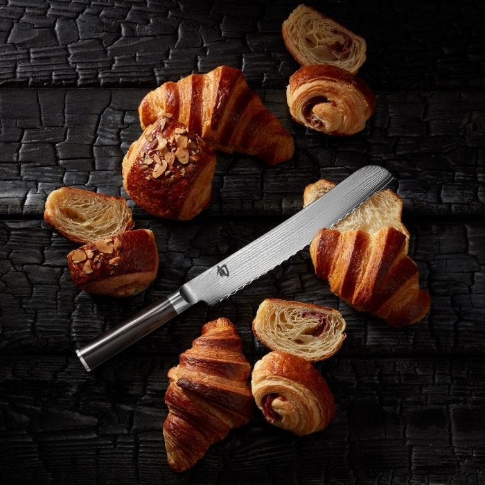 Shun | Classic Bread Ebony knife with serrated edge, surrounded by flaky croissants, showcasing its precision in slicing delicate pastries without crushing.