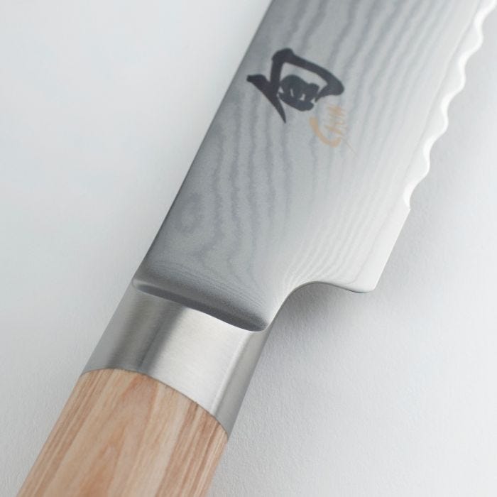 Shun | Classic Blonde Bread Knife, 9 inches: Close-up of the laminated, scalloped stainless steel blade with Japanese etching and a light-colored wooden handle.