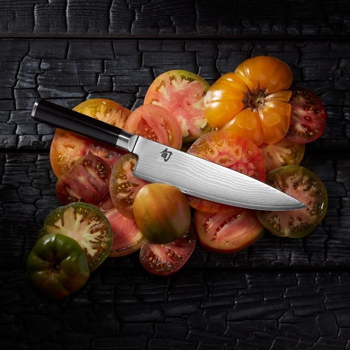 Shun | Classic Chef's Ebony, 8 inches knife rests on heirloom tomatoes, showcasing its Damascus pattern and ergonomic handle, epitomizing precision and elegance for versatile kitchen use.