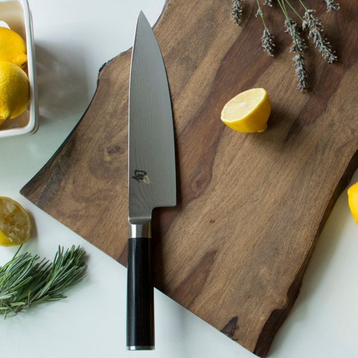 Shun | Classic Chef's Ebony, 8 inches knife on a wooden board with lemons and herbs, highlighting its versatile, high-performance blade for efficient food prep.