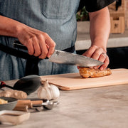 Shun Classic Chef's Ebony Knife, 8-inch, expertly slices chicken on a wooden board in a kitchen scene, highlighting its versatile, ergonomic design and superior cutting performance.