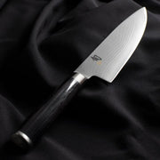 Shun Classic Chef's Ebony, 8-inch knife with Damascus blade and dark wooden handle, displayed on black fabric. Ideal for versatile cutting tasks.