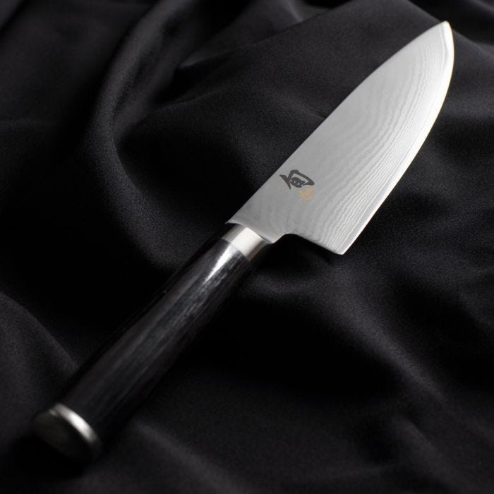 Shun Classic Chef's Ebony, 8-inch knife with Damascus blade and dark wooden handle, displayed on black fabric. Ideal for versatile cutting tasks.