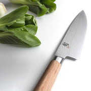 Shun | Classic Chef's Blonde, 8 inches knife with a Damascus-patterned blade and light wooden handle, displayed alongside fresh bok choy on a white surface.