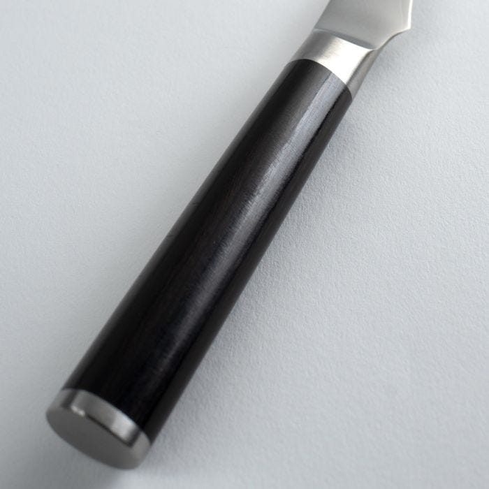 Close-up of Shun Classic Bird's Beak Paring knife's polished black handle, featuring a metal end cap and ferrule, ideal for precise decorative cuts.