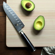 Shun Classic Hollow Ground Santoku knife on a wooden cutting board with avocado halves, showcasing its precision and versatility for all cutting tasks.