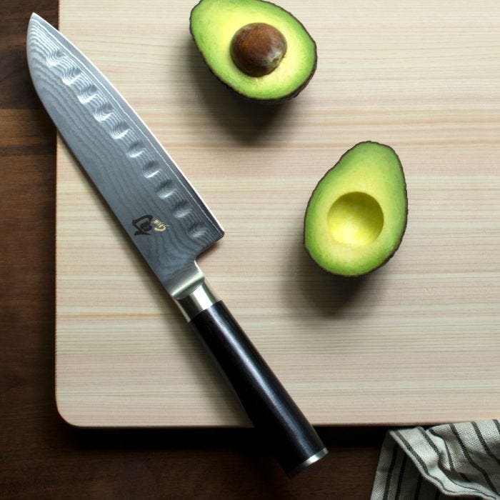Shun Classic Hollow Ground Santoku knife on a wooden cutting board with avocado halves, showcasing its precision and versatility for all cutting tasks.