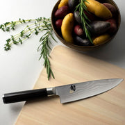 Shun | Classic Chef's Ebony, 6 inches knife on a wood cutting board with multi-colored fingerling potatoes and fresh herbs, showcasing its versatile culinary use.