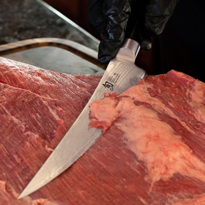 Shun | Classic Boning & Fillet, 6 inches: A gloved hand trims beef with a sharp, narrow Shun knife, ideal for precise meat and fish preparation.