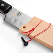 Shun Classic Hollow Ground Brisket Knife partially sheathed in beech-wood saya with red cord, showcasing craftsmanship ideal for precise meat slicing.