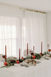 Mo&Co Home - Burgundy Dipped Beeswax Taper Candles elegantly accent a modern tablescape with red blooms, greenery, and black holders, perfect for seasonal gatherings.