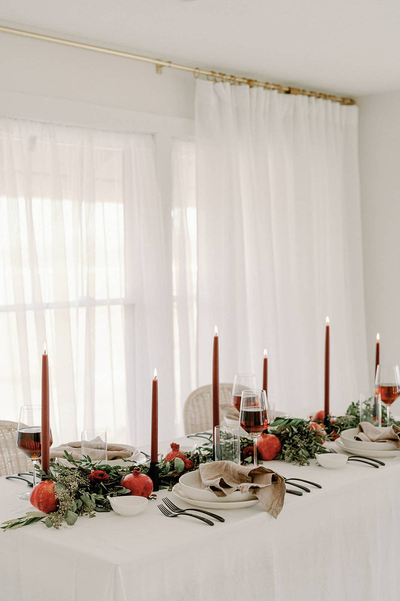 Mo&Co Home - Burgundy Dipped Beeswax Taper Candles elegantly accent a modern tablescape with red blooms, greenery, and black holders, perfect for seasonal gatherings.