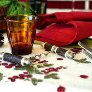 Couleur Nature - Gooseberry Red & Green tablecloth with red berries, greenery, and rustic holiday accents, complemented by an amber glass and wooden-handled corkscrew.