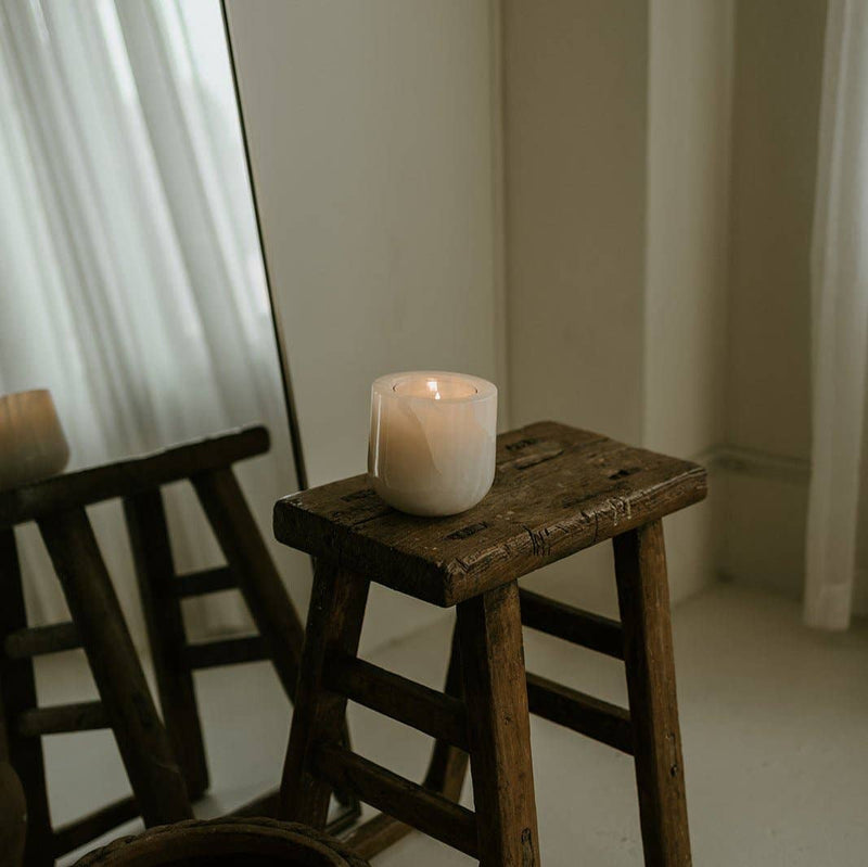 Last Candle Co - White Onyx Refillable Candle on a wooden stool; a minimalist setting with sheer curtains and a mirror, highlighting its elegant ceramic vessel.