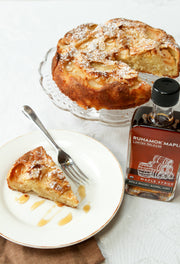 Runamok - LIMITED RELEASE Apple Brandy Barrel-Aged Organic Maple Syrup next to a rustic fruit-studded cake slice, showcasing a perfect pairing for fall delights.