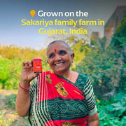 A woman smiling, holding a small box labeled Diaspora Co. Spices - Hariyali Fennel, showcasing its premium quality from Athens Cooks' specialty food selection.