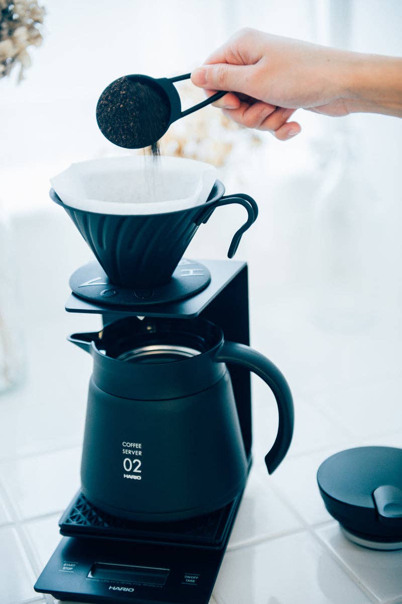Preparing coffee with HARIO USA - V60 Metal Dripper: Silver, showcasing its precise brewing features atop a Coffee Server 02 on a digital scale.