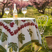 Couleur Nature - Fig Red & Green tablecloth on a round table with wine, enhancing an outdoor picnic ambiance with a bistro chair and basket nearby.