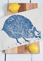 Hearth and Harrow - Organic Cotton Guinea Hen Tea Towel in Navy Blue draped over a wooden cutting board with two lemons, showcasing artisanal design.