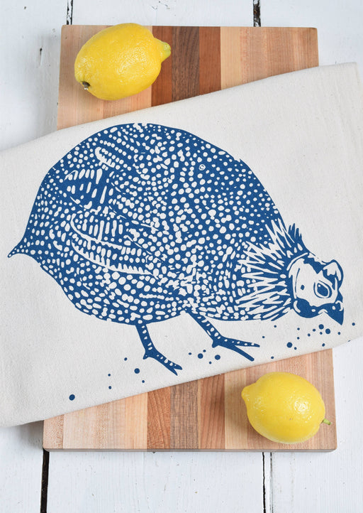 Hearth and Harrow - Organic Cotton Guinea Hen Tea Towel in Navy Blue draped over a wooden cutting board with two lemons, showcasing artisanal design.