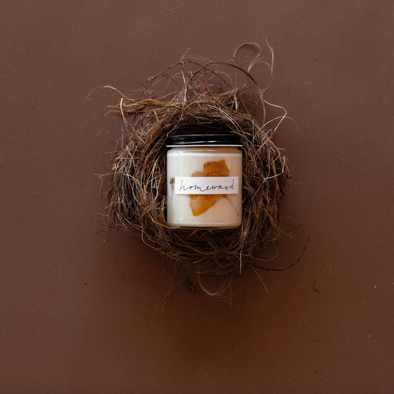 Among the Flowers - Essential oil candle | HOLIDAY: Hearth nestled in a bird-nest bowl, featuring ivory soy wax with amber decor.