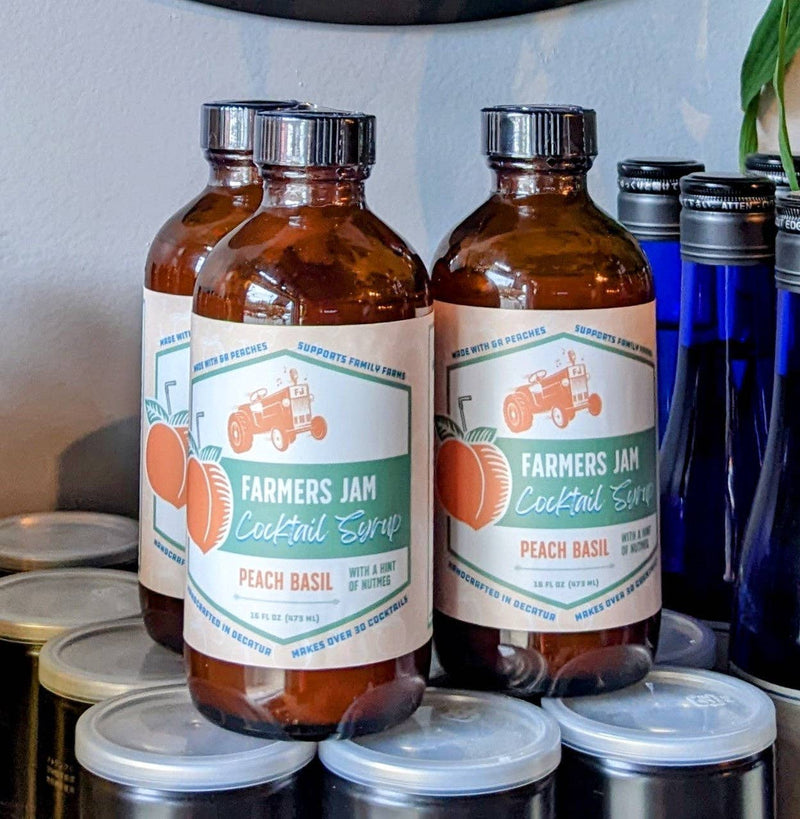 Farmers Jam | Peach Basil Cocktail Syrup - 8oz bottles, featuring a tractor logo, displayed on metal tins, ideal for cocktails. Perfect for enhancing drinks with a sweet, aromatic blend.