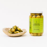 Villa Jerada - Picholine Olives - 7oz: Moroccan Picholine olives in a jar with herbs and red onion bits on a dish, celebrating traditional Moroccan flavors.