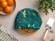 Bee's Wrap - Assorted 3 Pack - Oceans, featuring a pie wrapped with a blue cloth, alongside a silver spatula and a bowl of oranges on a wooden surface.