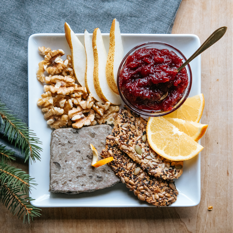 Beth's Farm Kitchen - Cranberry Sauce - Low Sugar! on a snack board with pâté, walnuts, pears, crispbreads, orange slices, and evergreen garnish.