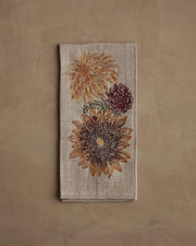 Coral & Tusk - Autumn Sunflower Tea Towel: A folded linen tea towel with embroidered sunflowers and a burgundy mum, showcasing autumnal hues.