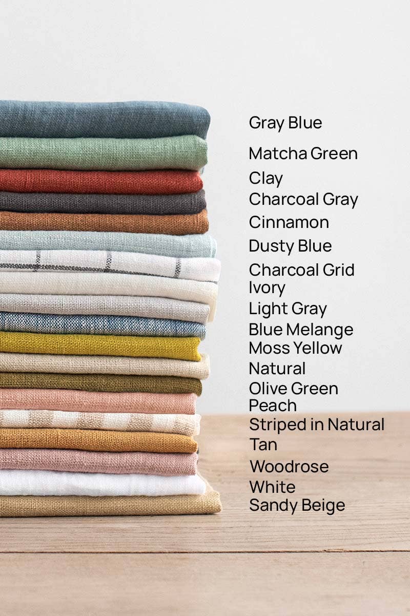 MagicLinen Charcoal Grey Linen Bib Apron with Pockets, showcasing a stack of colorful fabric; ideal for cooking and gardening.