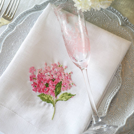 Arte Italica & Crown Linen Designs - Hydrangea Tri-Fold Napkin, featuring detailed hydrangea embroidery on linen, presented elegantly on a table setting with utensils.
