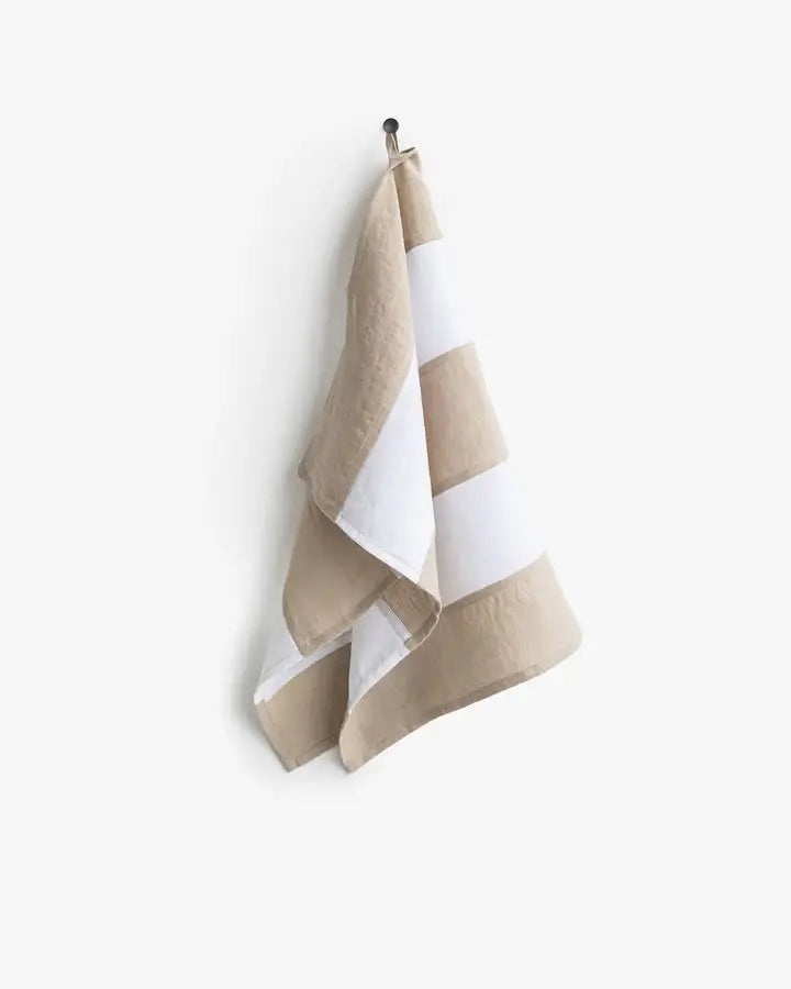 Striped Linen Tea Towel with hanging loop on hook, part of Athens Cooks' zero-waste program, crafted for durability and style in kitchen settings.