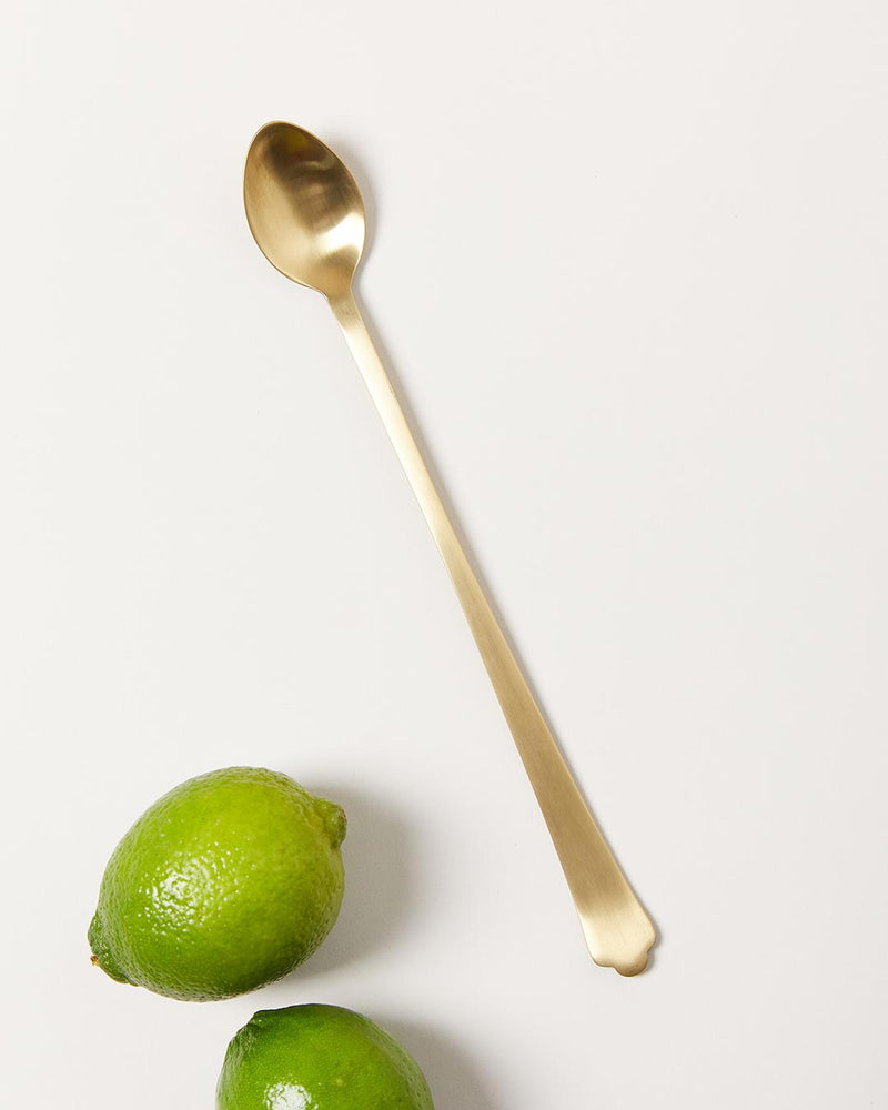 Farmhouse Pottery | Essex Barware, Long Spoon - Brushed Gold, displayed with two limes, ideal for mixing cocktails, combining elegance and functionality for any bar setting.