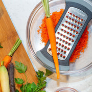 Microplane Bowl Graters, Extra Coarse, showcased grating carrots over a glass bowl, surrounded by colorful carrots and parsley, ideal for efficient meal prep.