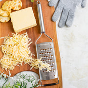 Microplane | Professional Series Extra Coarse Cheese Grater on a cutting board with cheese, crackers, and a cut-resistant glove, showcasing its robust design and functionality.